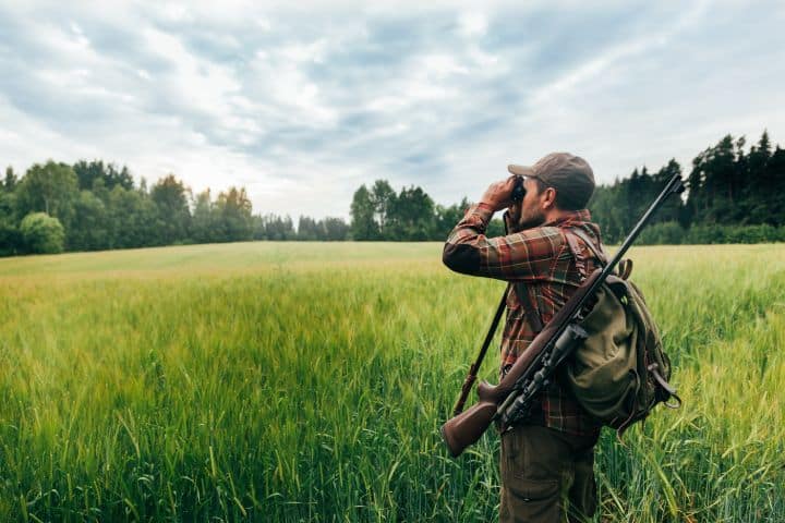 Alabama Hunting License Agent Bond - A hunter with his gun, bag, and binoculars scope in an open field.