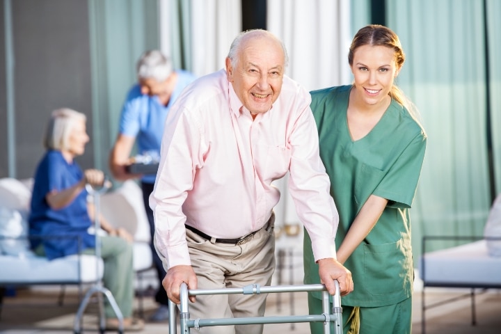 FL - Nursing Home Patient Trust Bond - A female caretaker helping senior man in using Zimmer frame.
