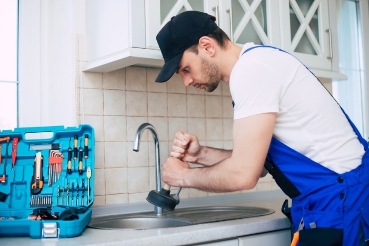 Osceola County, FL - Plumbing Contractor Bond ($5,000) - Handyman in uniform cleaning a clogged kitchen sink.