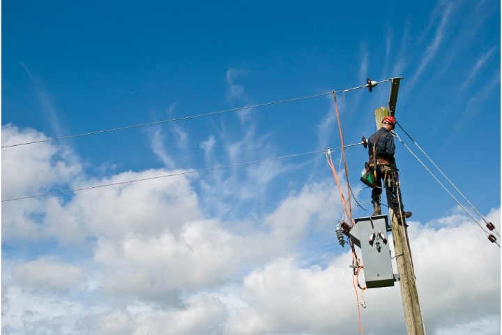 City of Tallahassee, FL - Utility Deposit Bond - Utility worker repairing power lines under a blue sky.