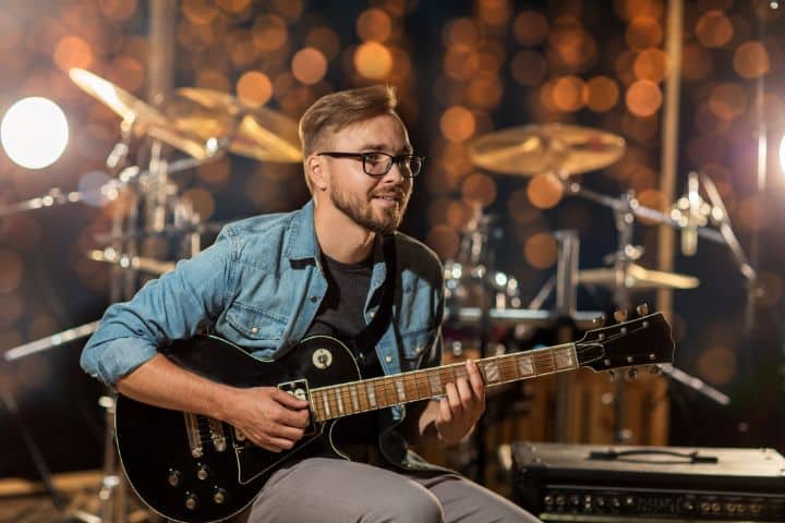 California Talent Agency $50,000 Bond - Musician playing guitar with a background of bokeh lights and a drum set.