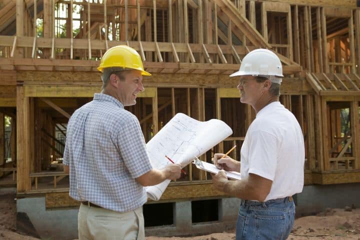 Contractors read blueprints by the frame of the building.