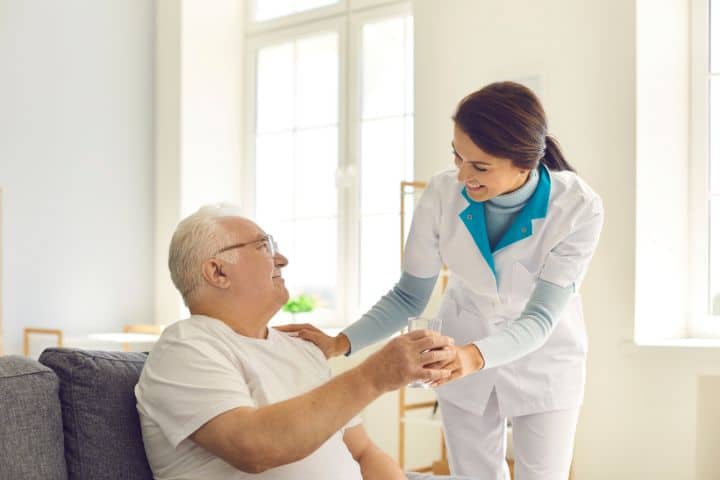 California Health Facility Patient Trust Fund Bond - Smiling nurse giving a glass of water to a senior man in a nursing home.