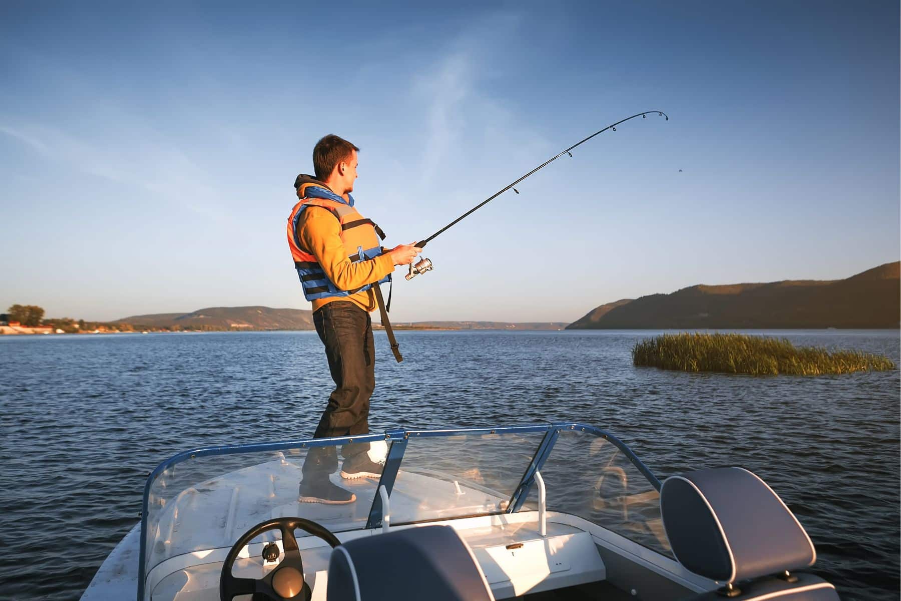 Young man fishing while at the boat and wearing life jacket.
