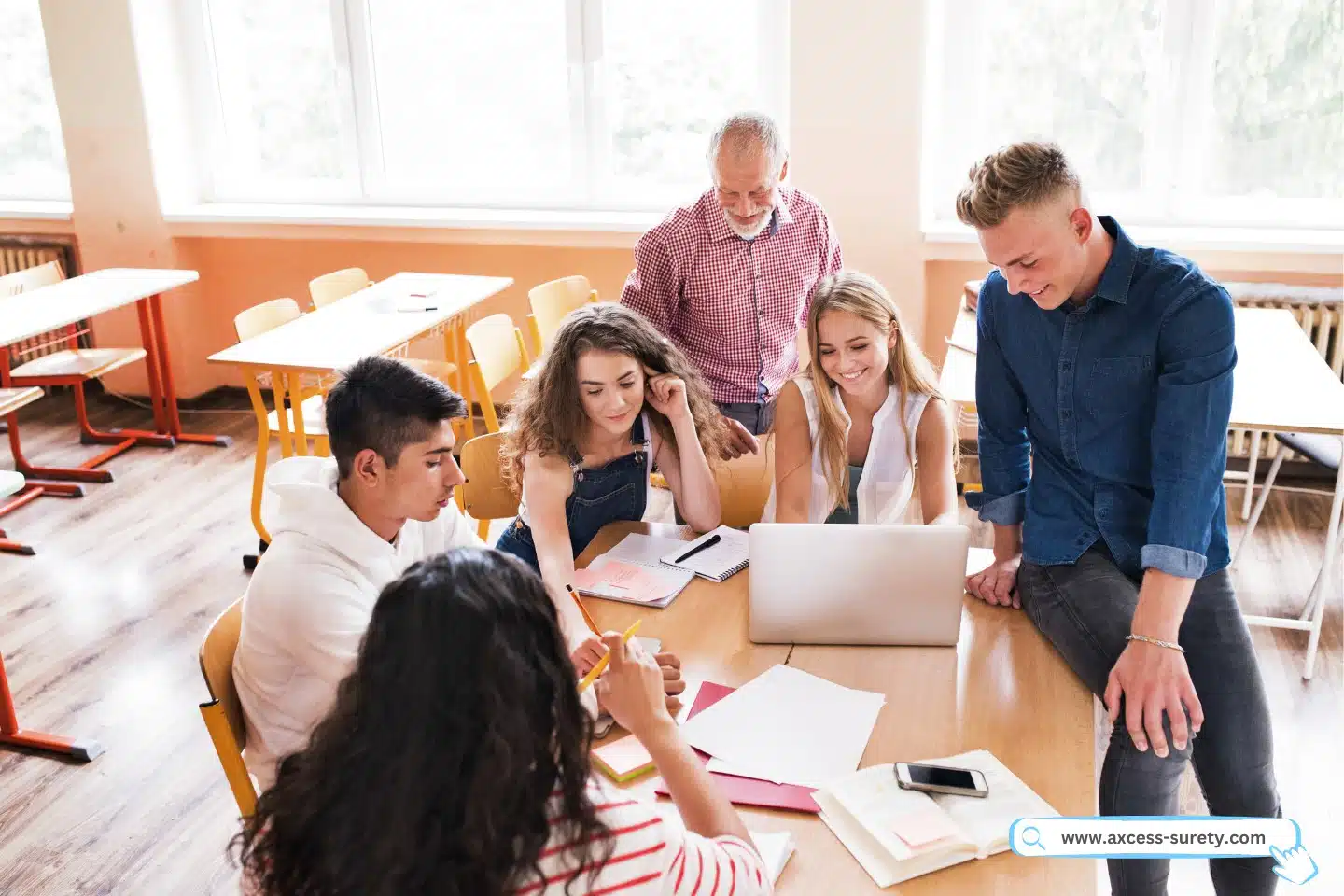 Inside the classroom, a group of high school pupils and their teacher are using laptops.