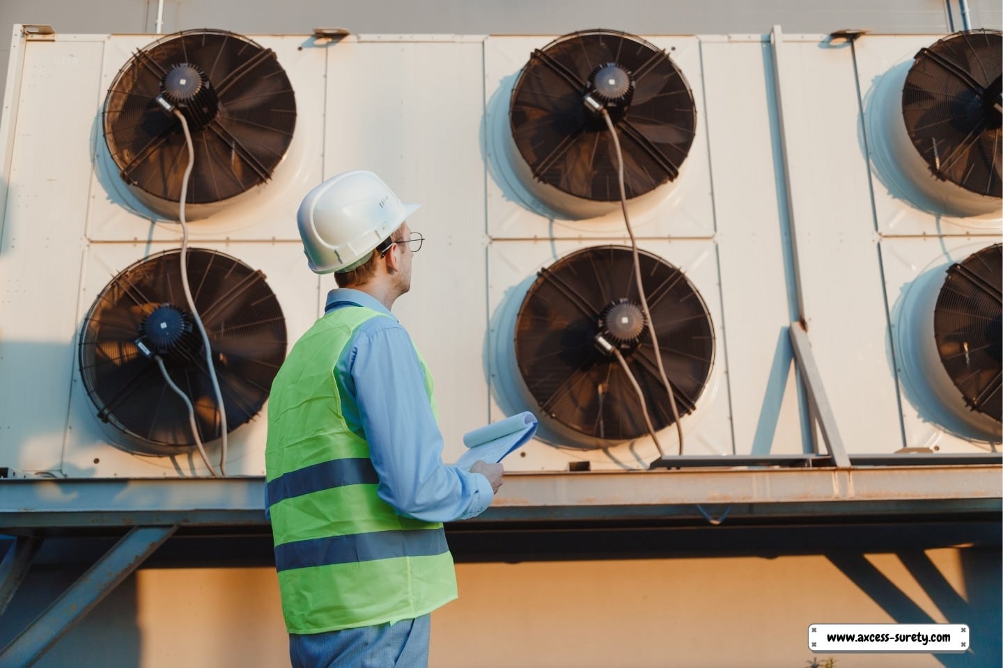 An industrial refrigeration system is inspected by a service HVAC engineer wearing a hard hat and uniform.