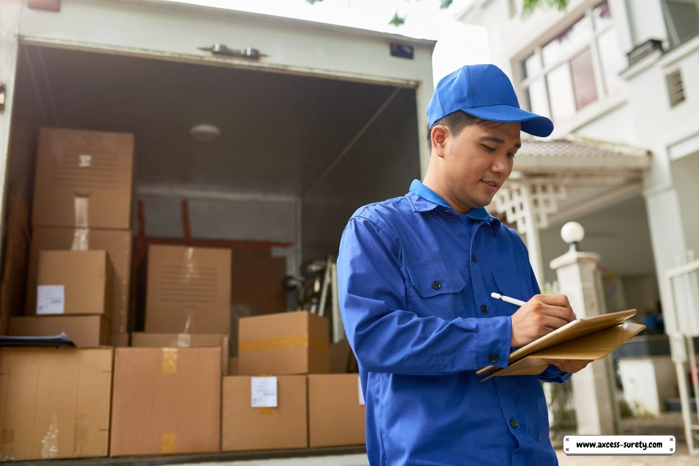 A moving business courier is filling out paperwork while standing at a delivery vehicle loaded with boxes.
