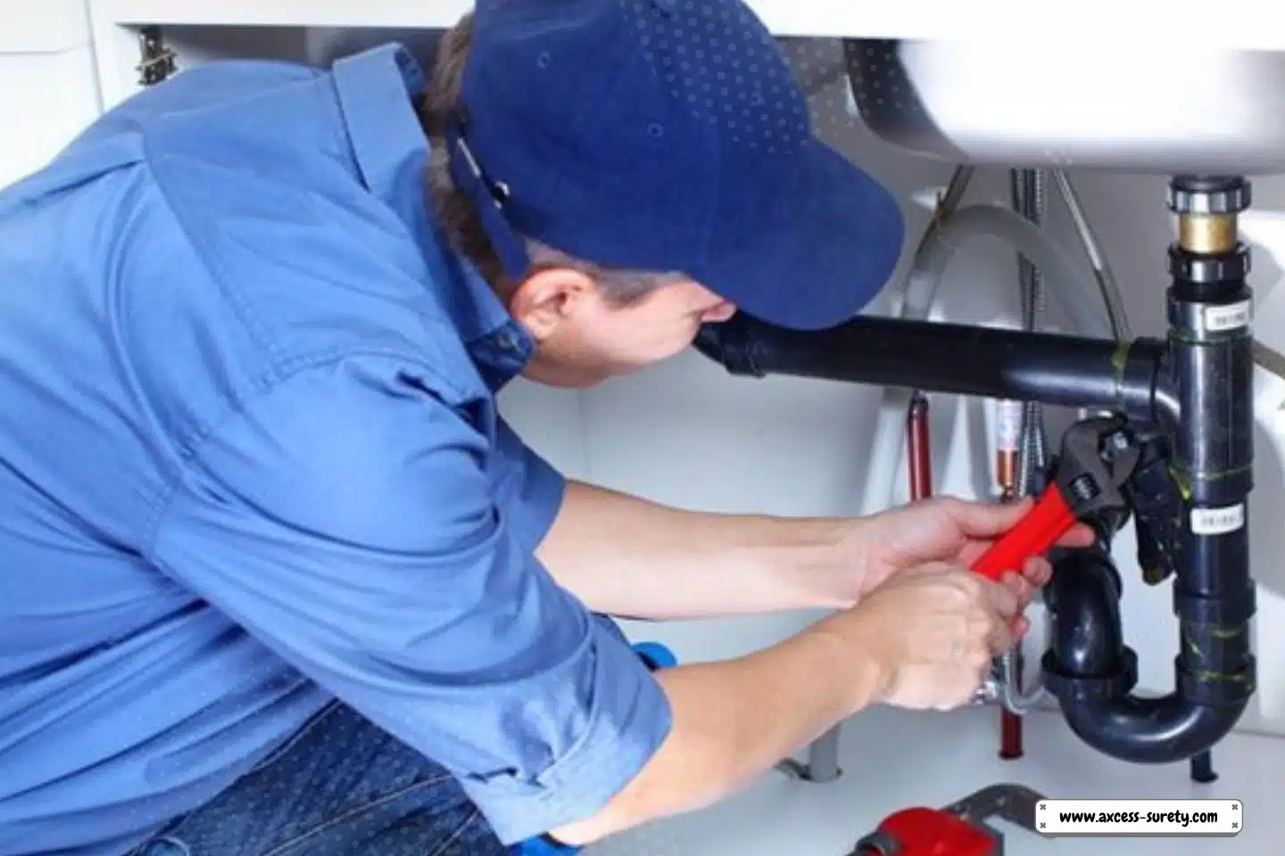 A plumber in blue uniform and cap fixing sink using red and black adjustable sink.