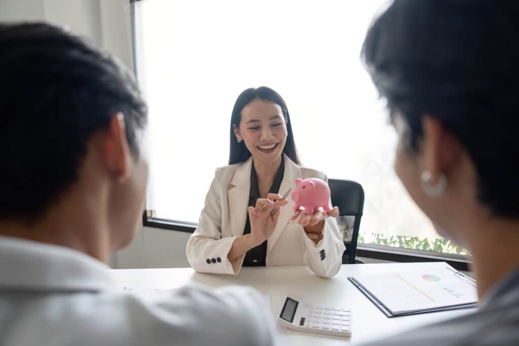 Financial advisor holding a piggy bank and explaining a savings plan to an LGBTQIA gay couple in a modern office setting
