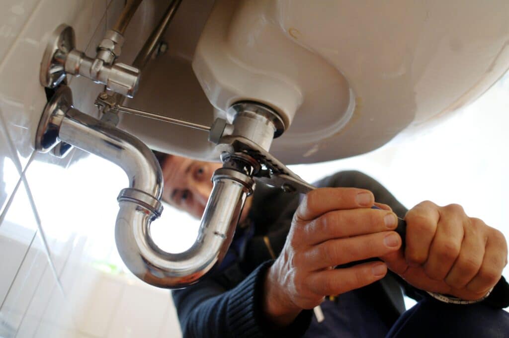 Close-up of plumber fixing sink. Male professional repairing appliance on wall in bathroom. He is working on equipment with metallic tool at home.