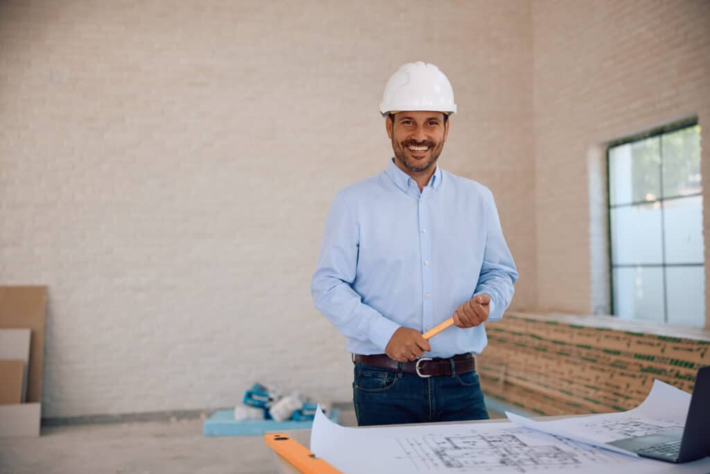 Happy architect analyzing blueprints at construction site and looking at camera. Copy space.