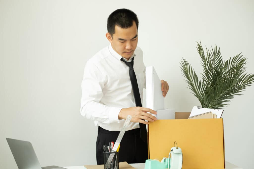 A male office worker is unhappy with being fired from a company packing things into cardboard boxes. The young man was stressed and disappointed by being fired. concept of layoffs and unemployment.