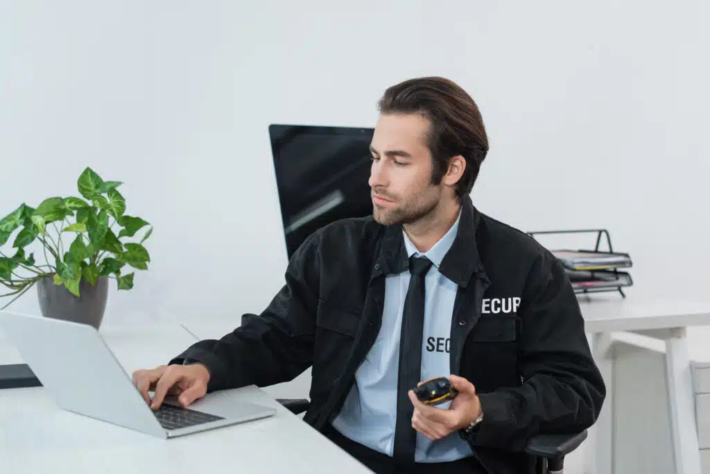 security man in black uniform holding walkie talkie and typing on laptop