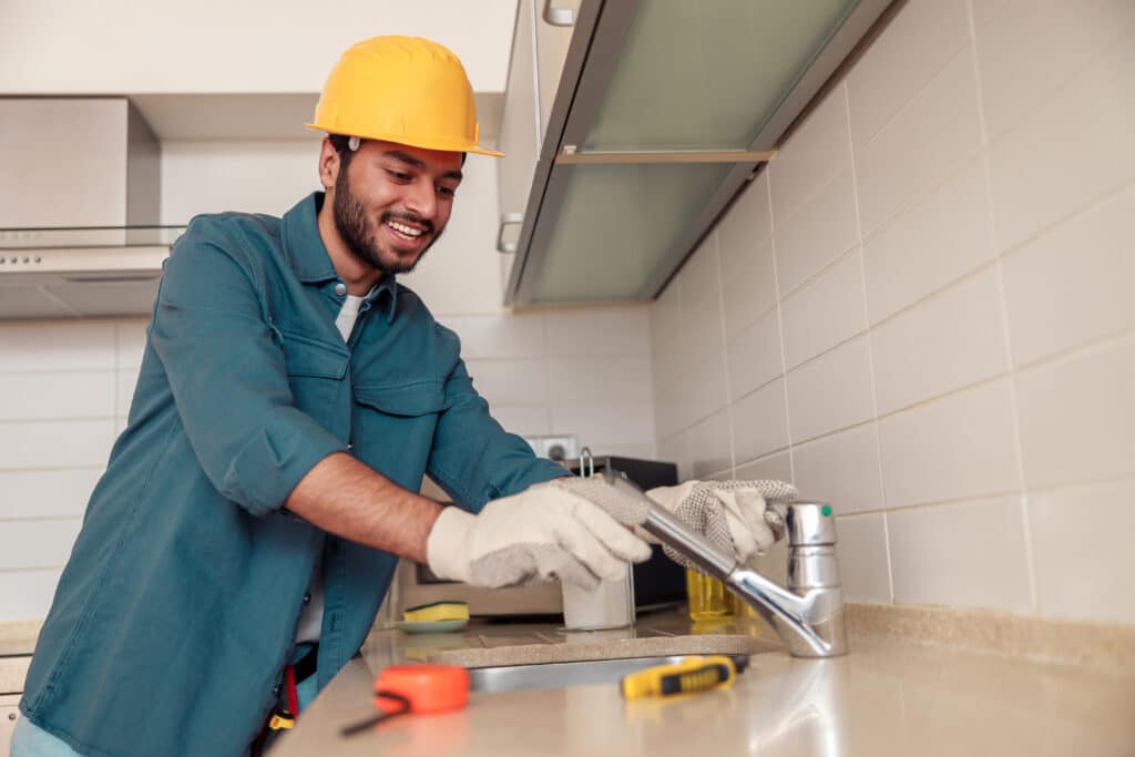 Male plumber repair sink faucet at customer kitchen. Maintenance and household assistance concept