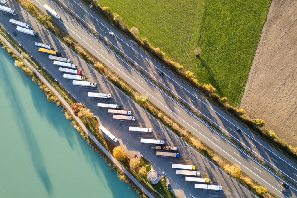 Top down aerial view of highway interstate road with fast moving traffic and parking lot with parked lorry trucks.