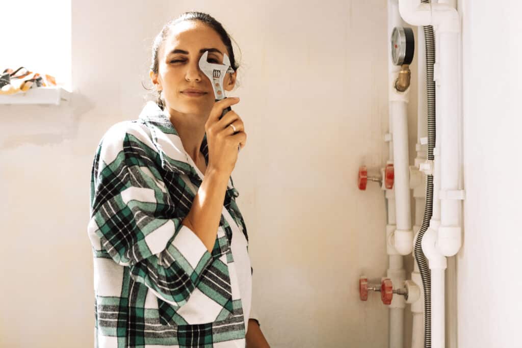 Young woman holds adjustable plumbing wrench near her face. Brunette repairs heating equipment or pipes. Charming girl is smiling and messing with construction tools. Renovation of apartment.