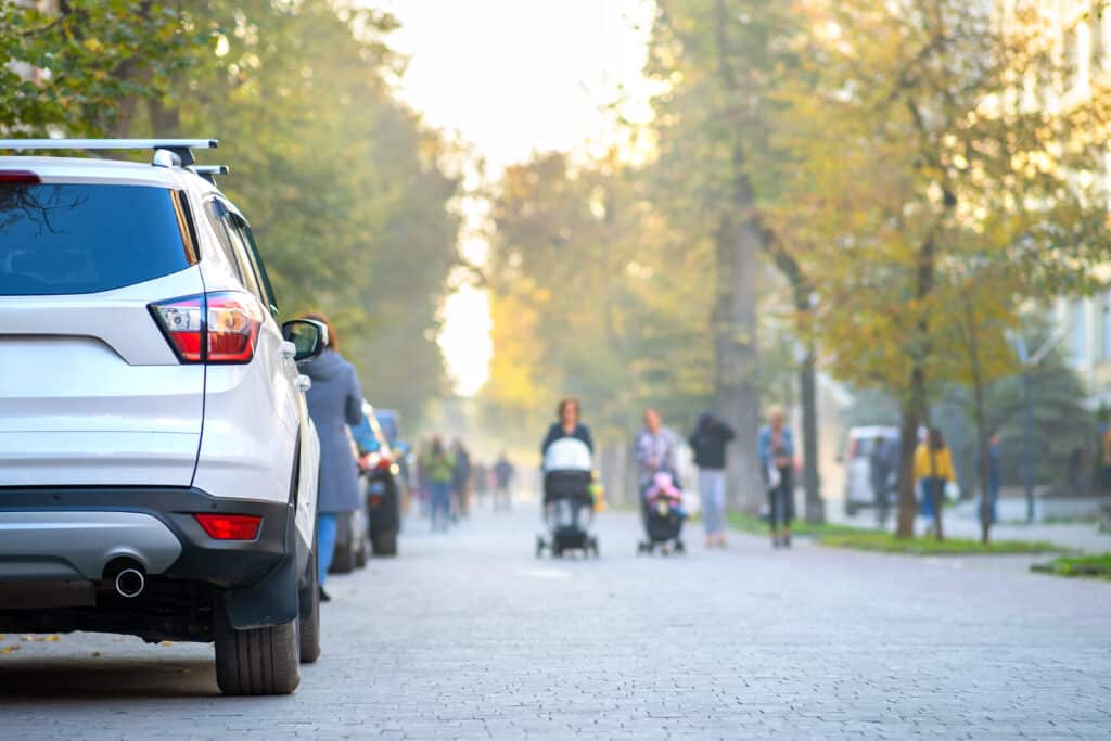 Car parked on a city street side on bright autumn day with blurred people walking on pedestrian zone.