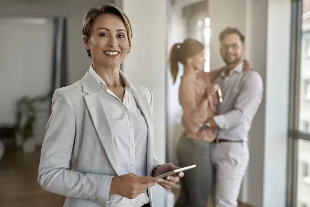 Portrait of happy real estate agent with a couple in the background.