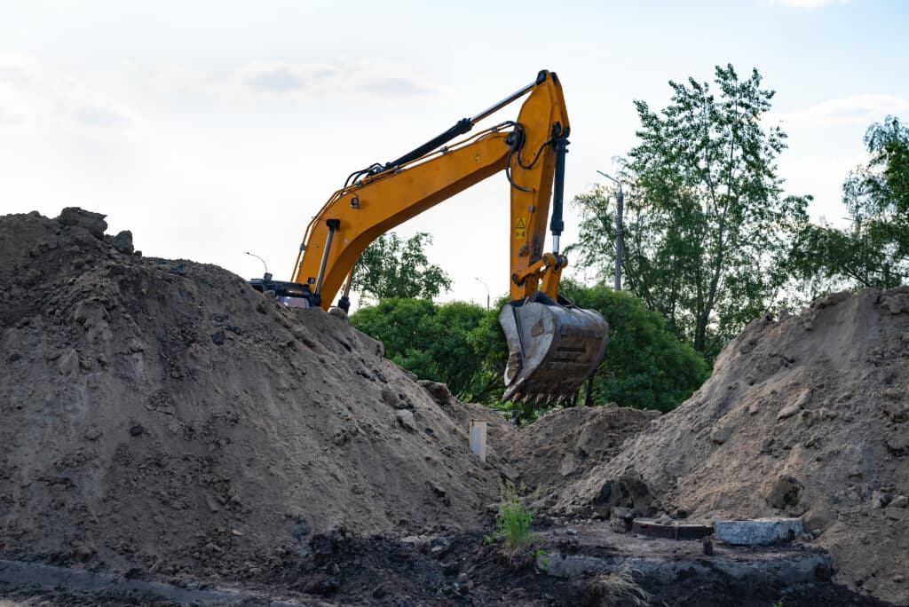 Excavator during earthmoving at open pit on blue sky background. Construction machinery and earth-moving heavy equipment for excavation, loading, lifting and hauling of cargo on job sites
