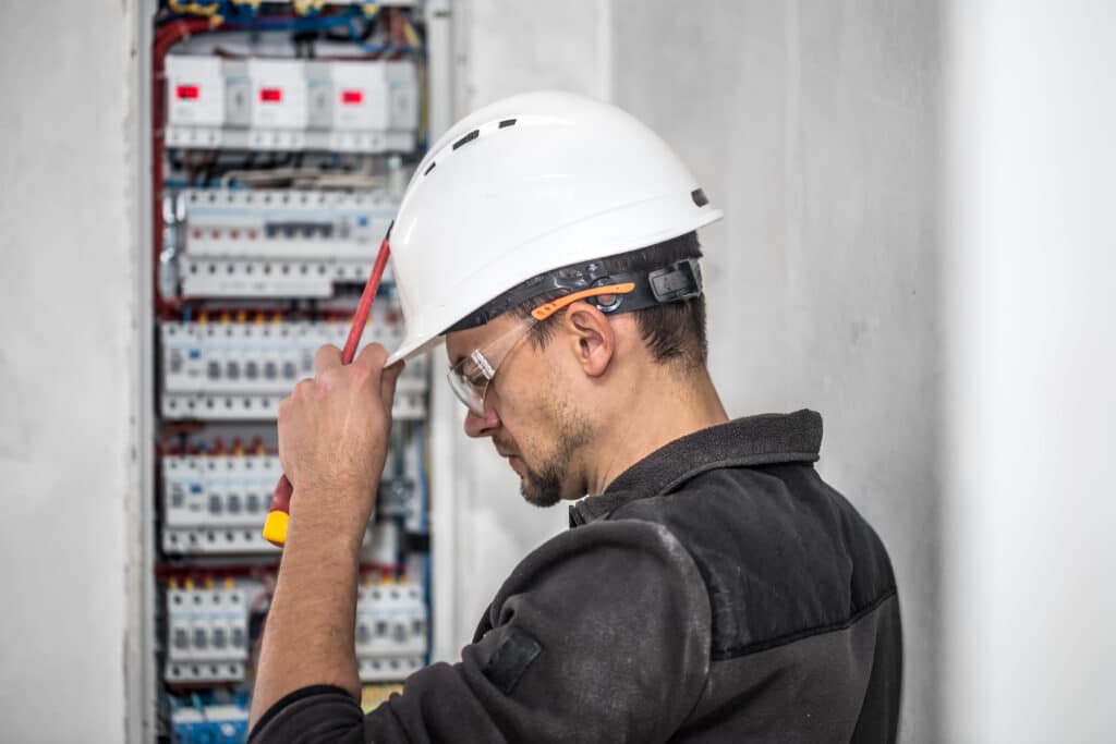 Man, an electrical technician working in a switchboard with fuses. Installation and connection of electrical equipment. Professional with tools in hand. concept of complex work, space for text.