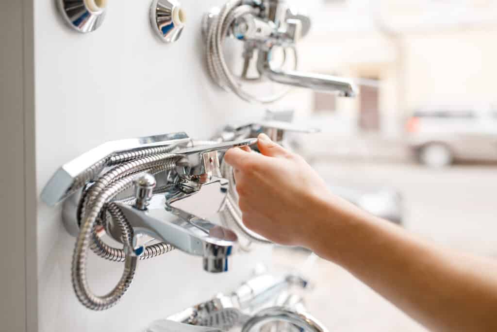 Plumber in uniform at showcase in plumbering store. Man with notebook buying sanitary engineering in shop, water taps and faucets choice