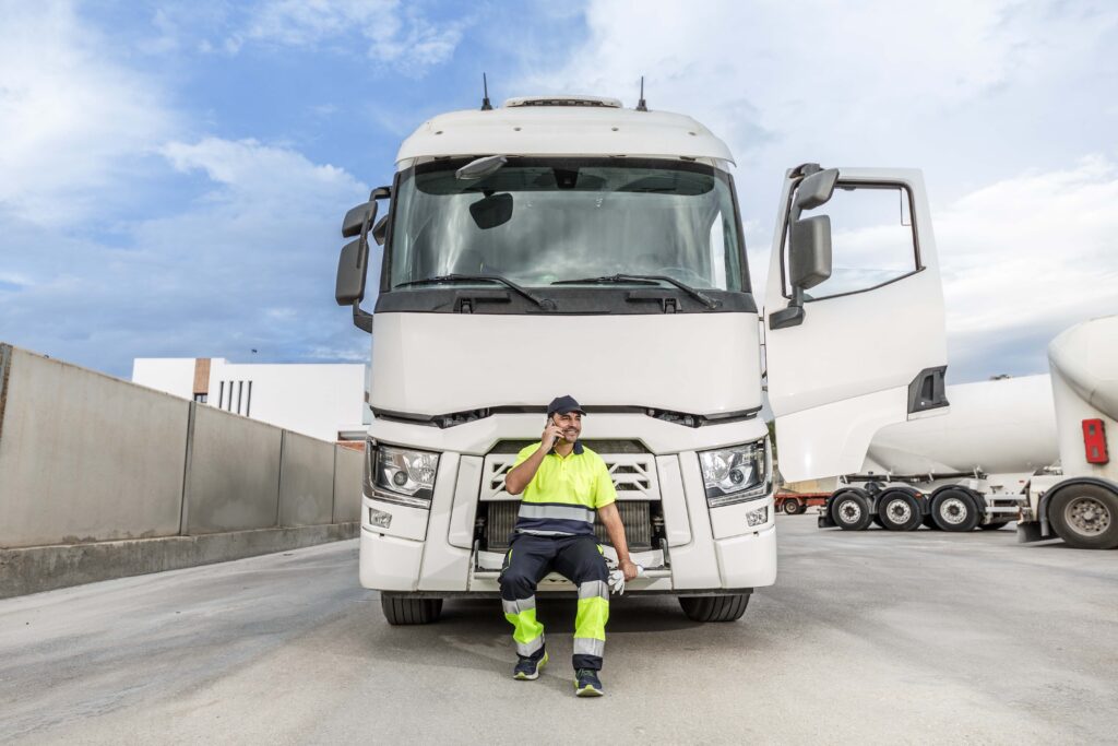 positive-male-driver-sitting-on-bonnet-of-truck-wh-2023-12-12-22-31-52-utc_11zon