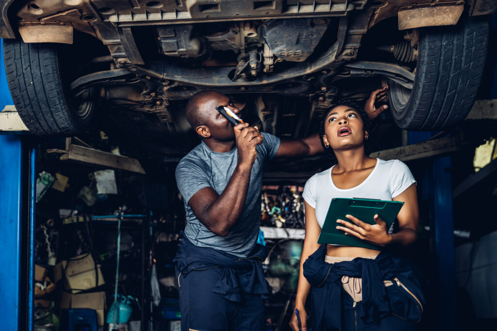 Professional Car Mechanic is Investigating Under a Vehicle on a Lift in Service. Auto Service Worker Checking Car Under Carriage Look For Issues. Car service technician check and repair customer car.
