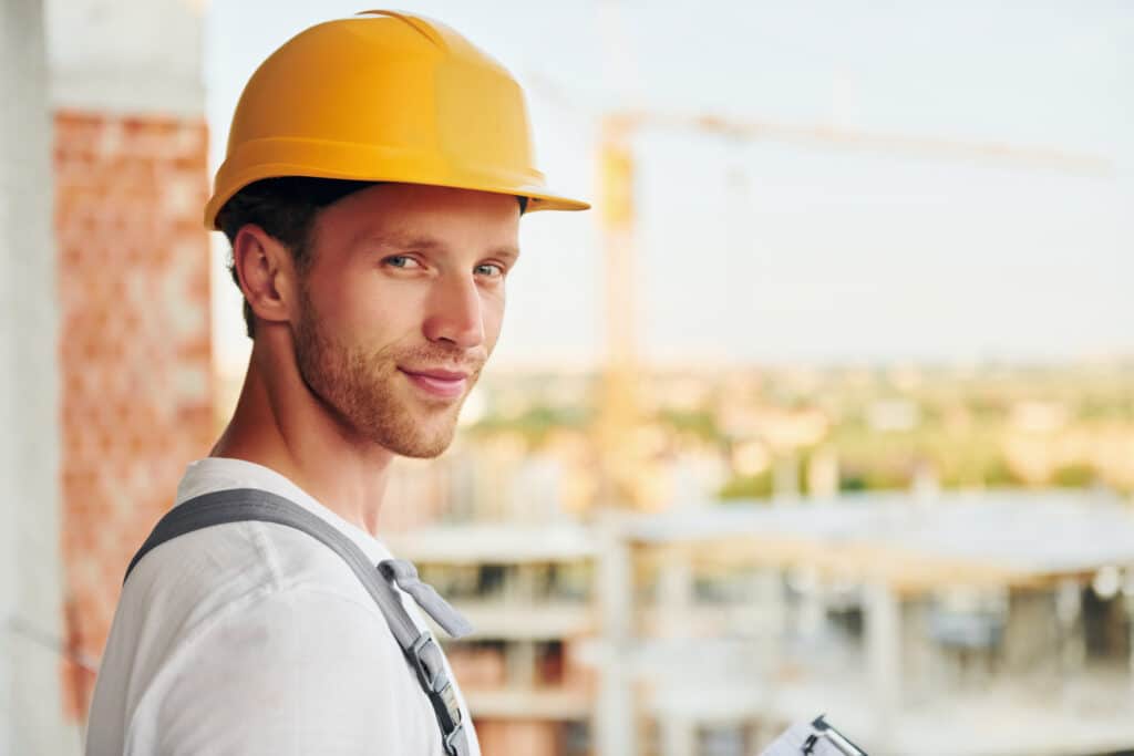 View from the side. Young man working in uniform at construction at daytime.