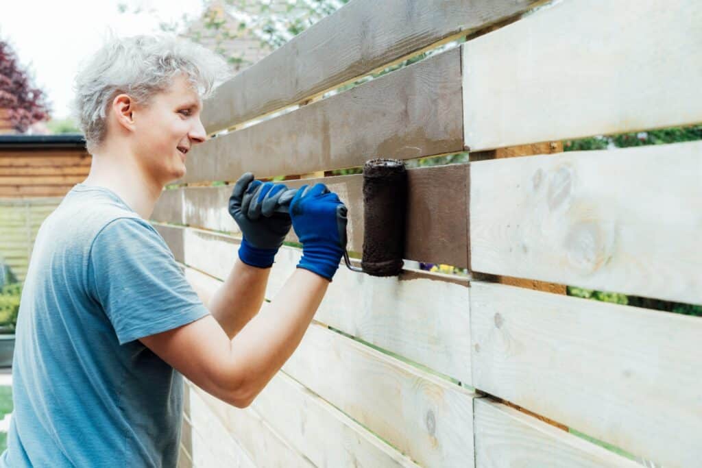 young-man-worker-paints-with-roller-a-wooden-board-2023-11-27-05-07-14-utc