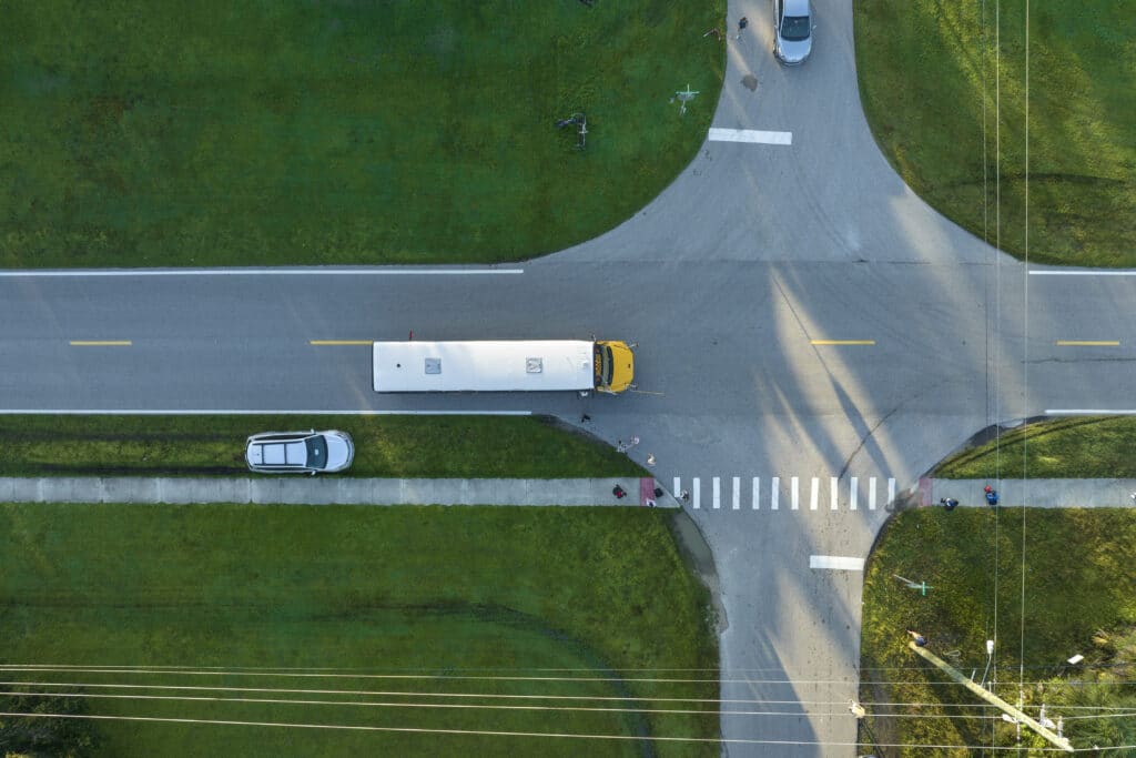 Aerial view of american yellow school bus picking up children at sidewalk bus stop for their lessongs in early morning. Public transportation in the USA.