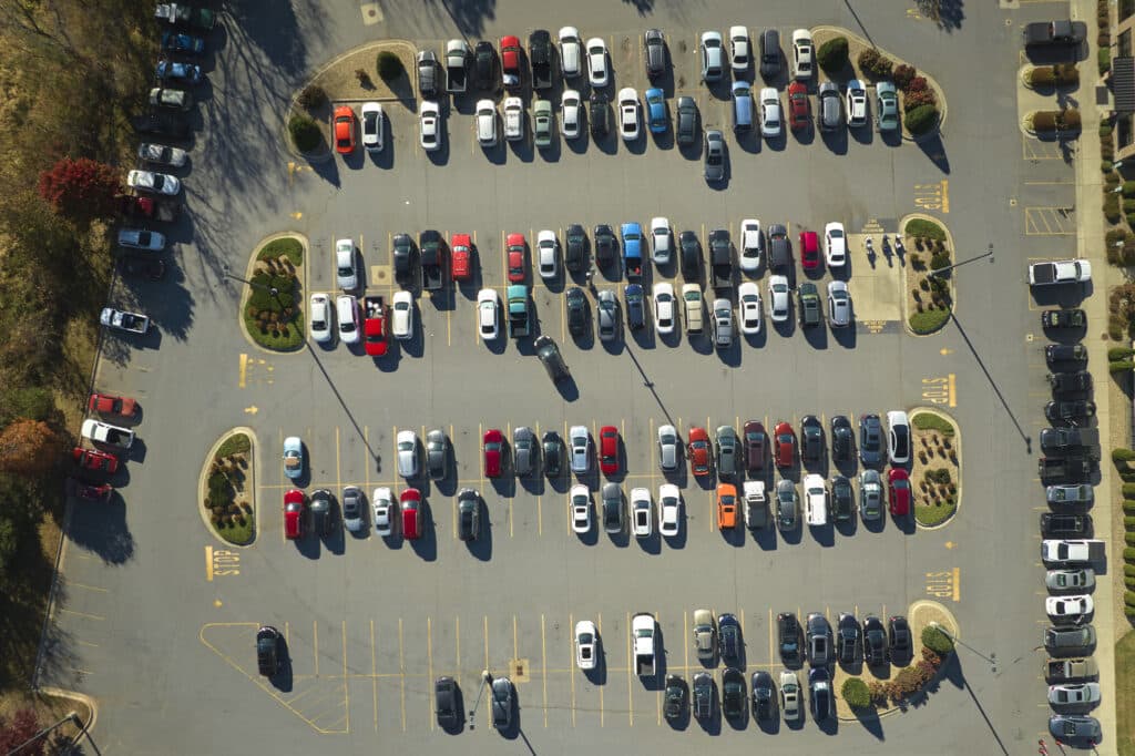 Aerial view of large parking lot with many parked colorful cars. Carpark at supercenter shopping mall with lines and markings for vehicle places and directions.