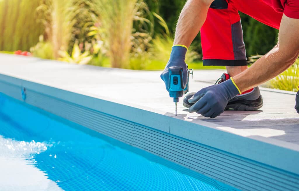 Caucasian Man Building Composite Swimming Pool Deck Inside His Backyard Garden. Drill Driver Close Up.