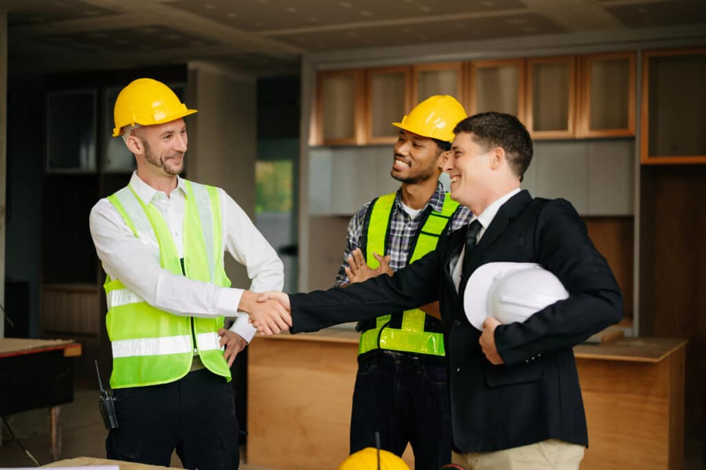 Engineers or architecture shaking hands at construction site for architectural project, holding safety helmet on their hands. successful cooperation concept