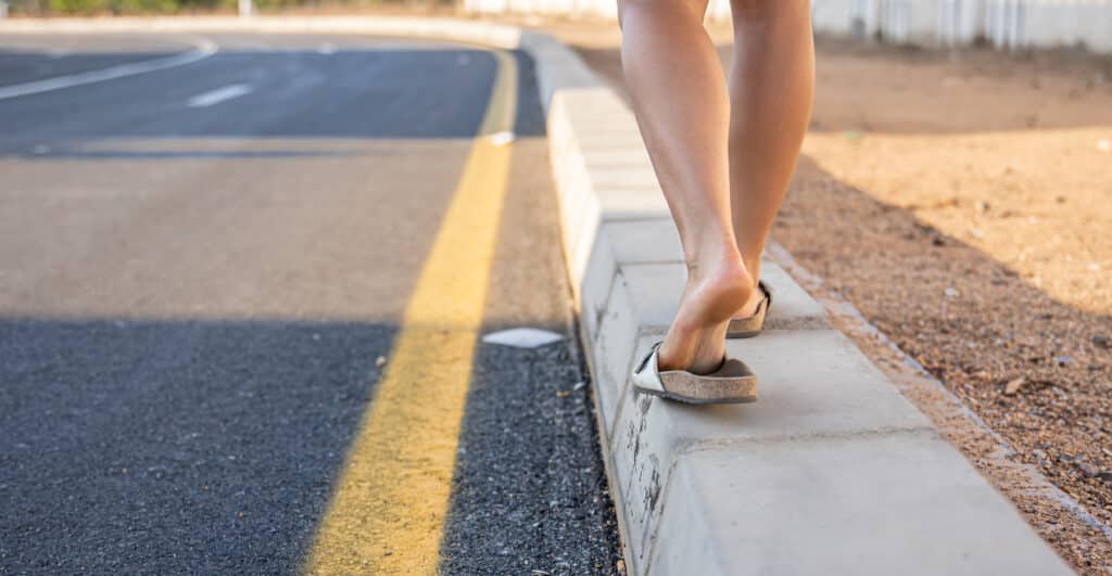 A girl with tanned legs walks along the sidewalk along the road close up.