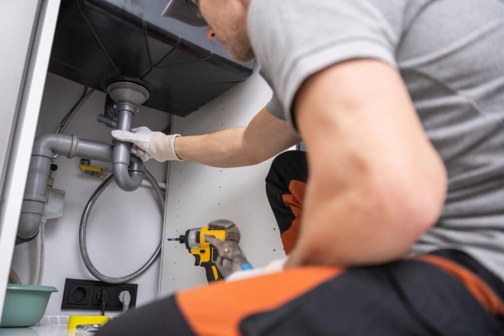 A plumber repairing a sink in the kitchen