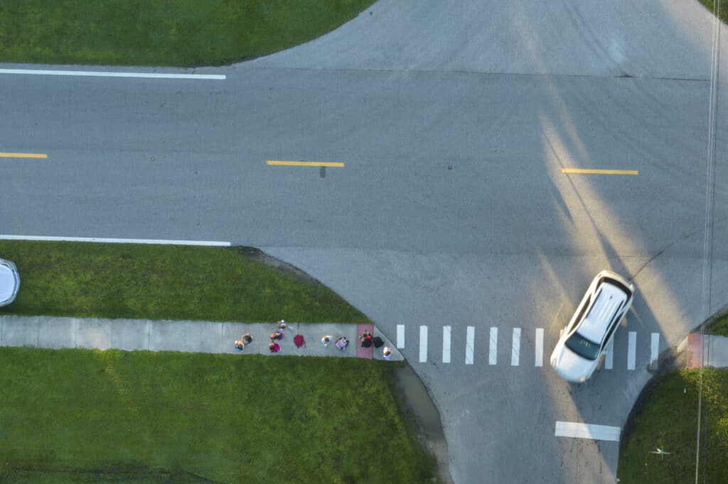 Top view of schoolkids waiting for school bus to arrive in time. Kids standing on suburban street sidewalk ready to be picked up in early morning. Public transportation in the USA.
