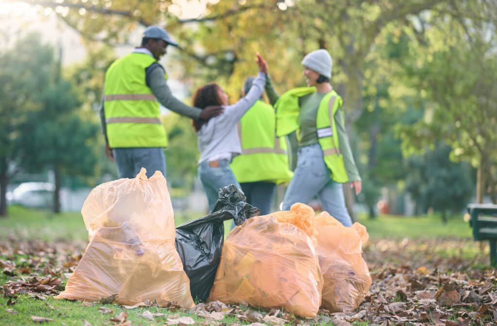 Volunteer, child and people high five while cleaning park with garbage bag for a clean environment