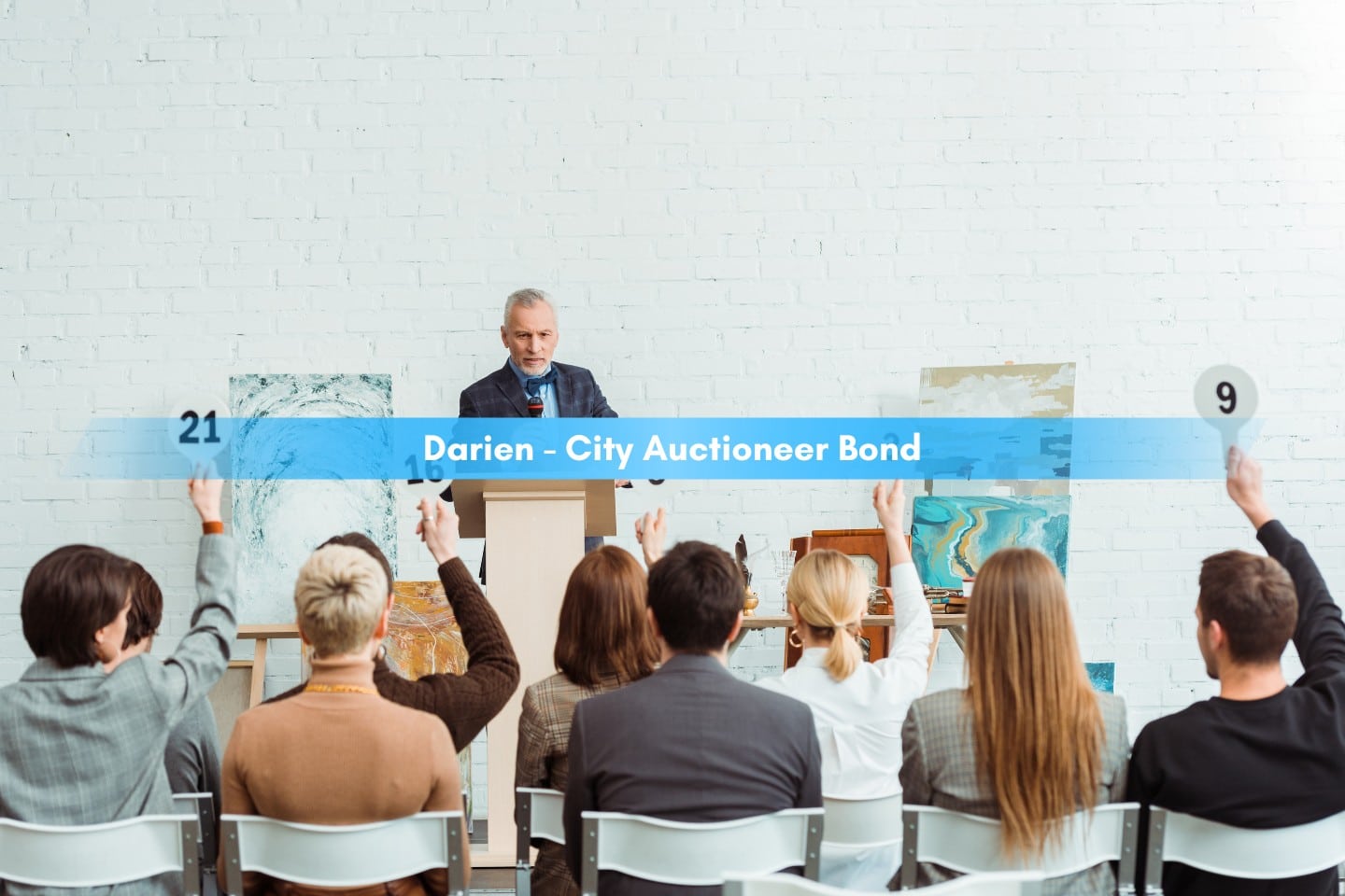 Darien - City Auctioneer Bond - Auctioneer talking and looking at buyers with auction paddles.