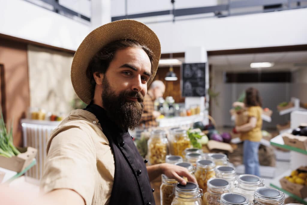 Smiling zero waste shop entrepreneur using selfie camera on cellphone to promote environmentally friendly vegan products online. Low carbon footprint supermarket owner filming marketing content