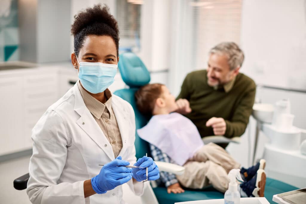 Happy African American stomatologist at dentist's office with her patients in the background.