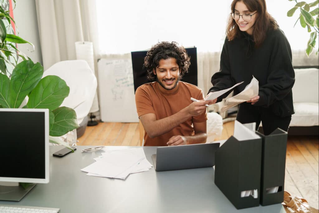 Mixed-race study session: European girl with notes, Indian male using a laptop