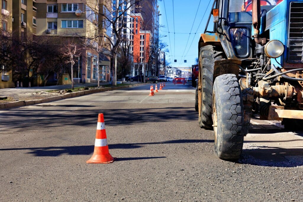 Orange traffic cones and an old tractor enclose a road repair area on a city street