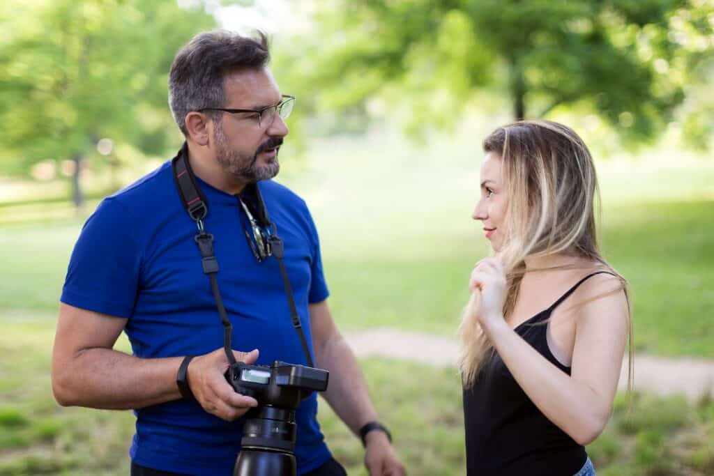 Photographer and model discuss the session of photo shoots. Natural outdoor scenery at the park, green background.