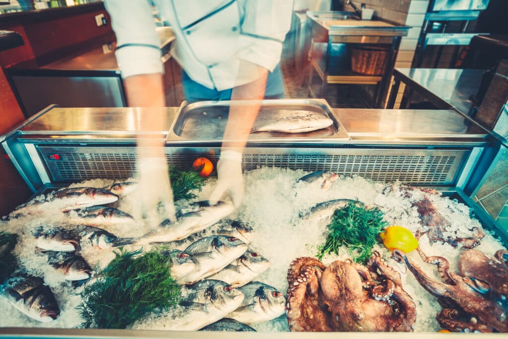 The chef-cooker is taking the freshly caught fish out of the refrigerated counter for the cooking delicious meal in the restaurant. Fresh seafood the fish and octopuses for healthy lifestyle.
