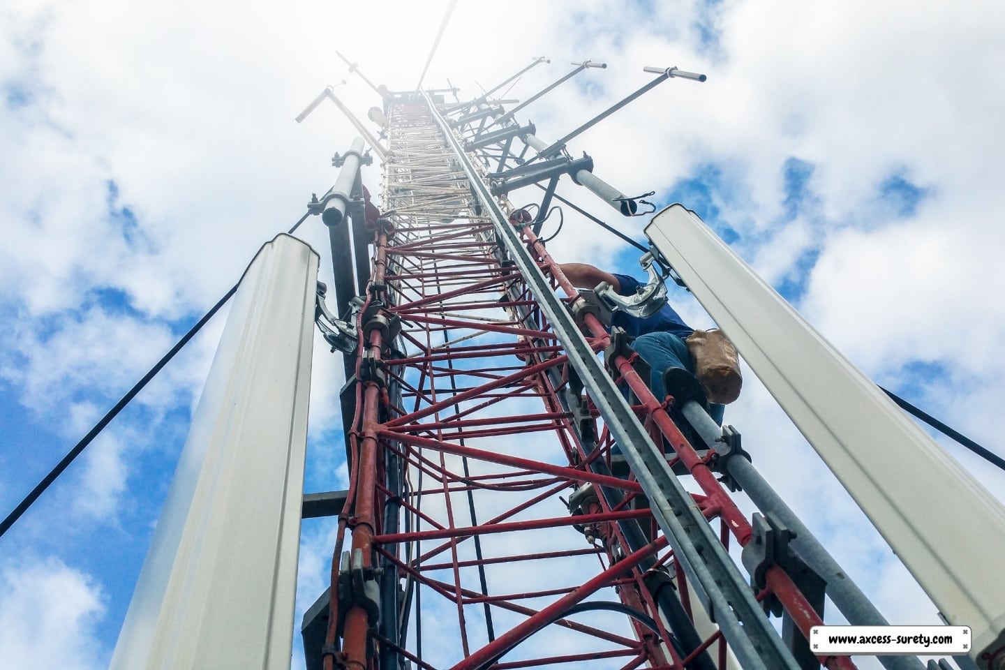 A worker ascends to the base station of an extremely tall metal construction radio cellular network antenna.