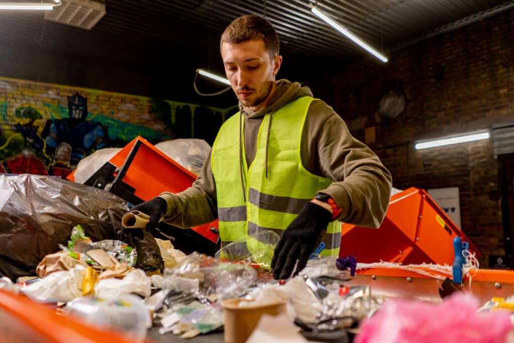 An employee in a uniform and gloves at a waste recycling station sorts and sorts garbage on a sorting line