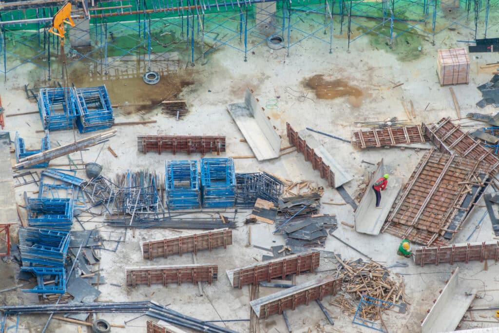 Aerial view of busy industrial under construction site workers working with cranes and excavators. Top view of precast concrete slap floor full of steel. Development high rise architecture building.