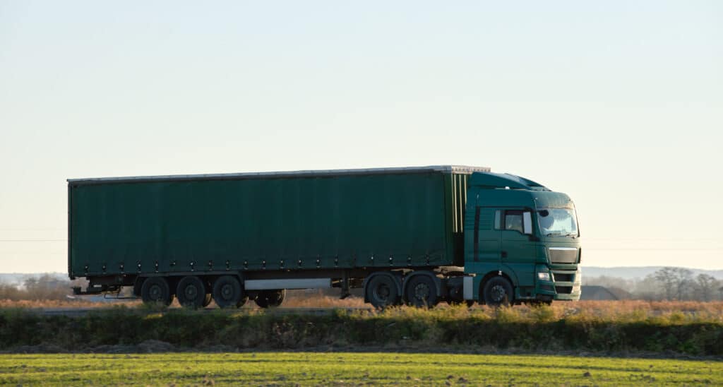 Semi-truck with cargo trailer driving on highway hauling goods in evening. Delivery transportation and logistics concept.
