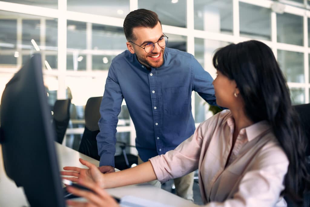 Caucasian man and woman freelancers discussing work in a coworking office while sitting at a computer. Colleagues are conferring at the expense of a startup.