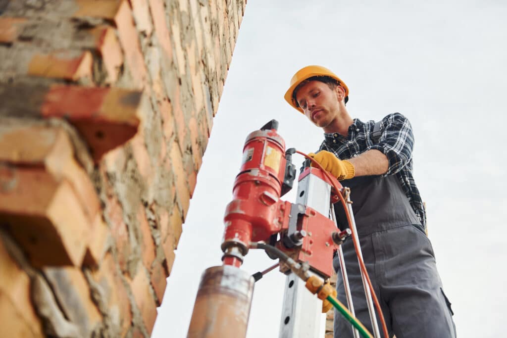 Uses blending drill. Construction worker in uniform and safety equipment have job on building.